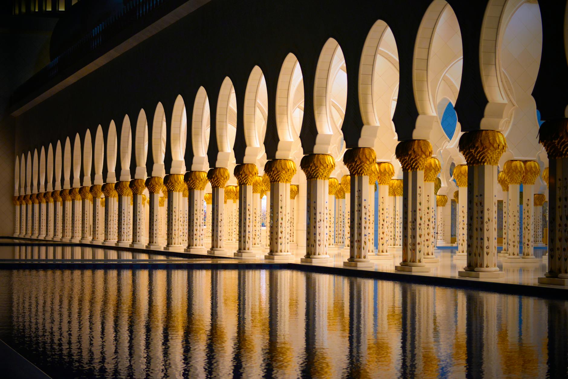 Glistening view of Sheikh Zayed Grand Mosque columns reflected in water at night.