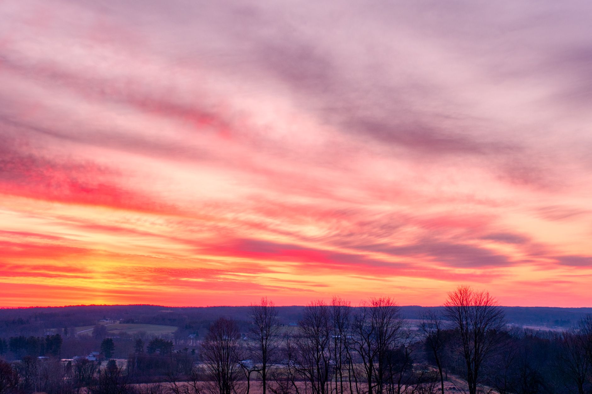 Low angle scenery view of colorful cloudy sky over leafless trees on hillside in wintertime at sunset