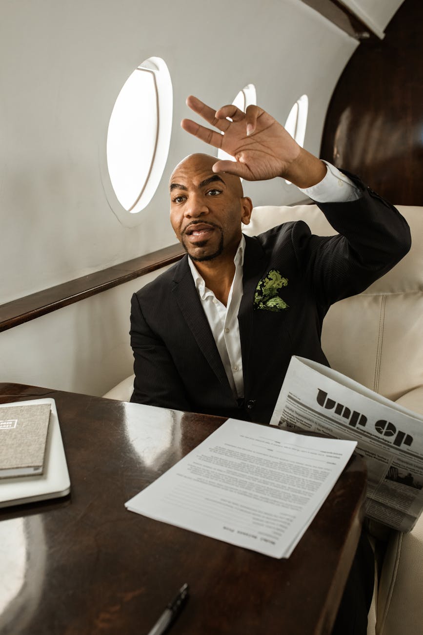 Elegant businessman sitting in a private jet cabin, reading a newspaper and making a gesture.