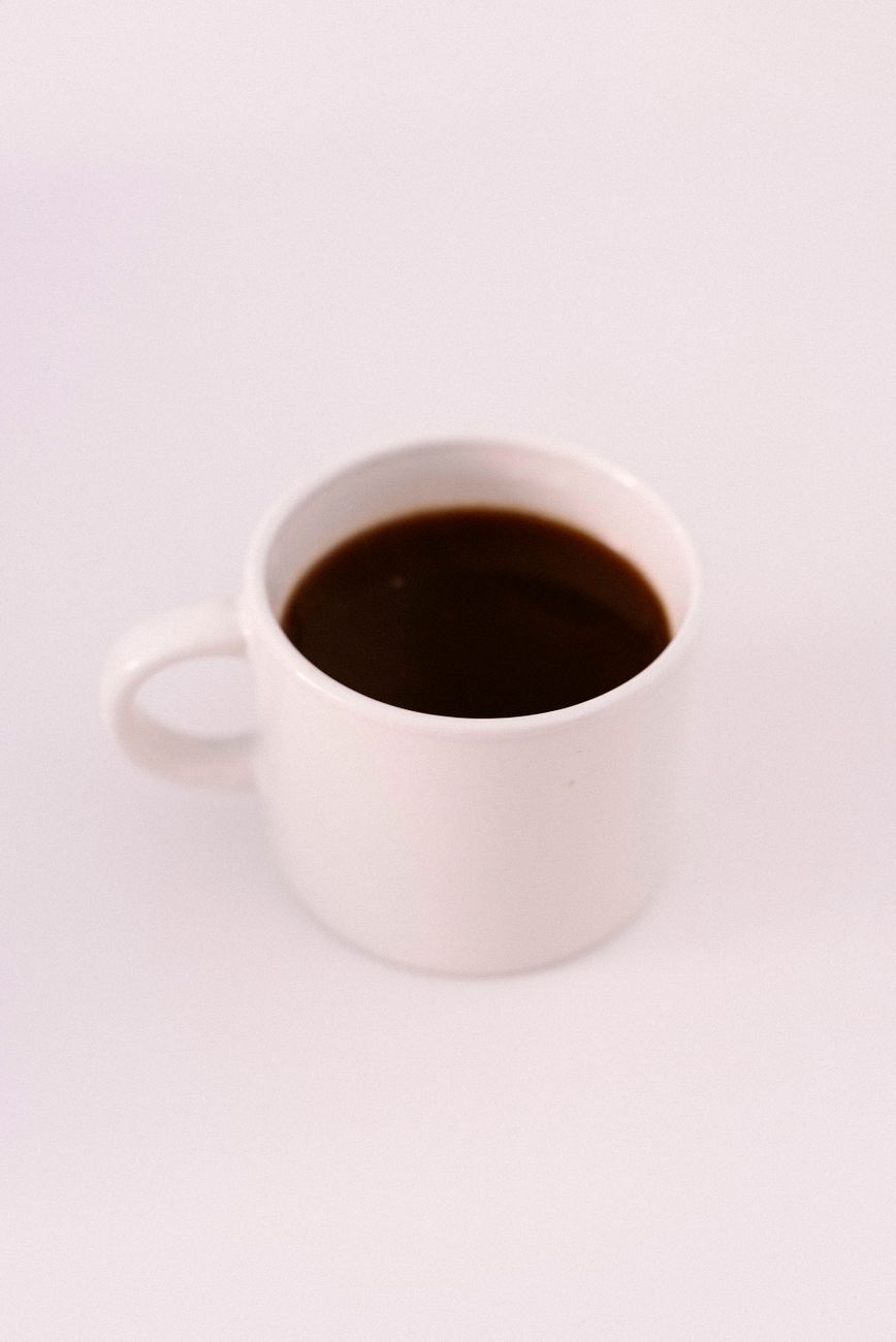 A simple and elegant white mug filled with black coffee against a plain background.
