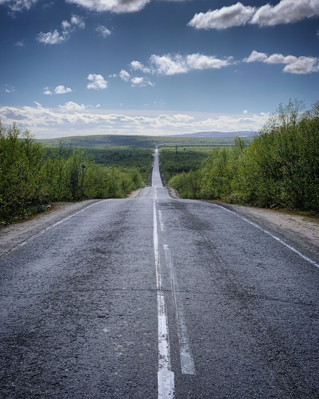 Endless road through lush Russian countryside under a vivid blue sky.
