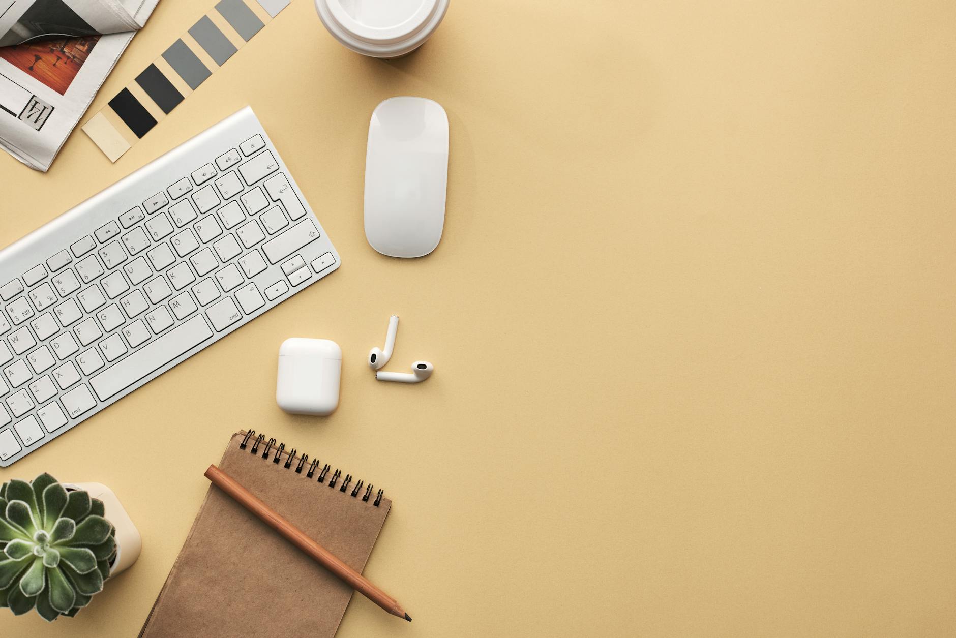 A minimalist workspace flat lay with keyboard, mouse, notebook, and succulent on a beige background.