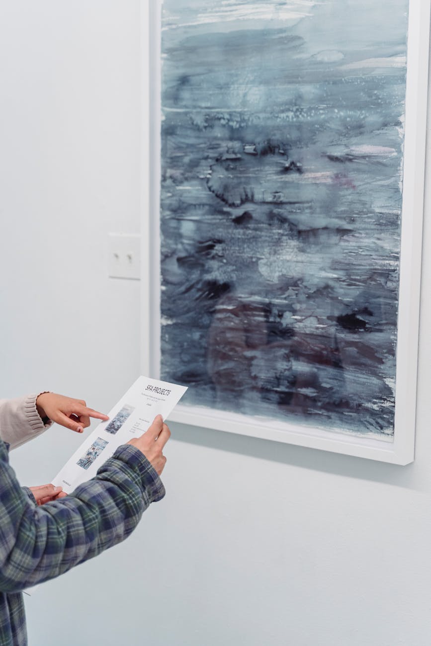 A visitor examines a brochure while admiring a blue abstract painting in a gallery.
