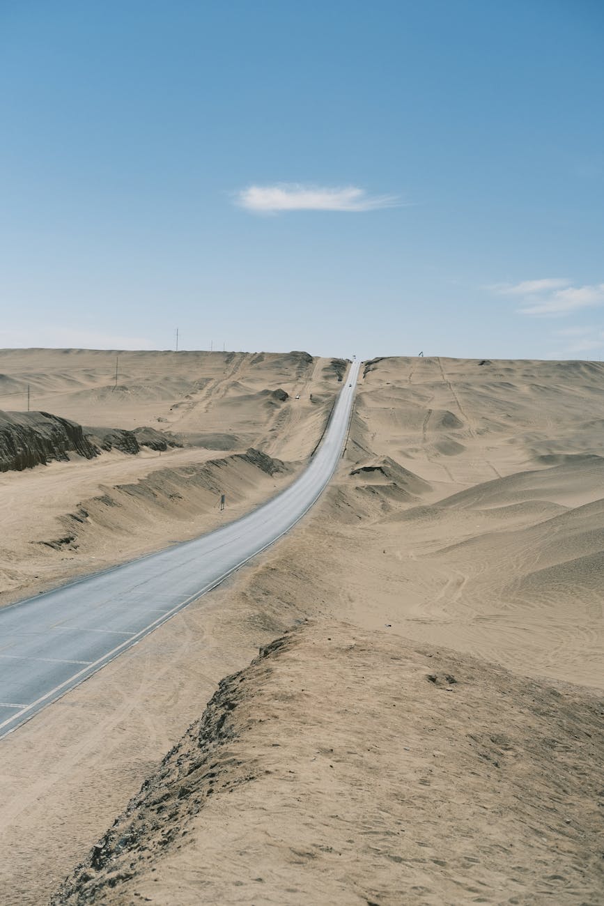 A long, empty road stretches through a barren desert landscape under a clear blue sky.