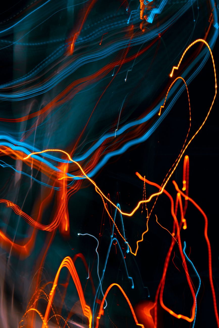 Abstract long exposure of orange and blue light streaks on a dark background.