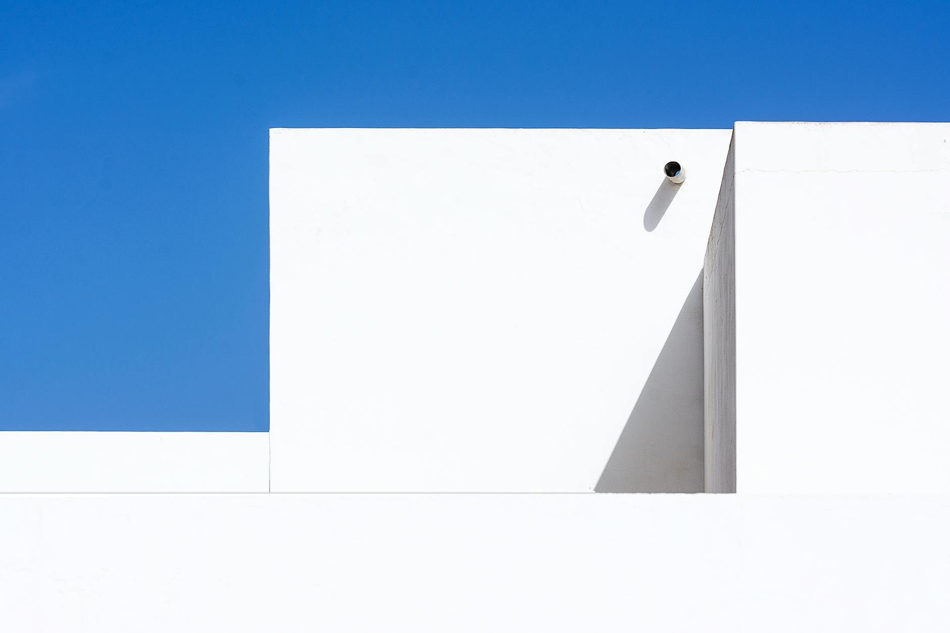 Abstract image of a white building with geometric shapes against a clear blue sky, casting shadows.