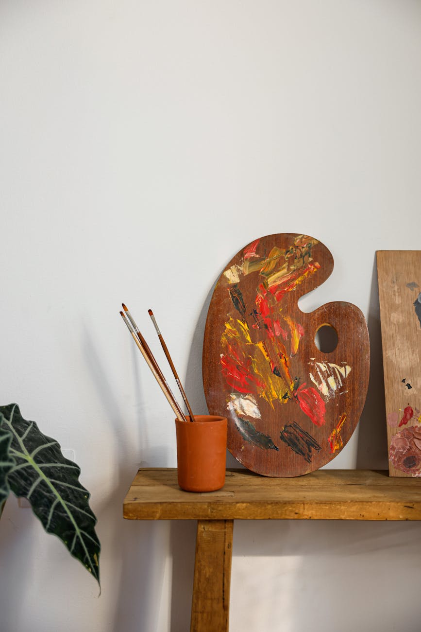 A wooden artist palette with vivid paint and brushes on a stool, embodying creative inspiration.