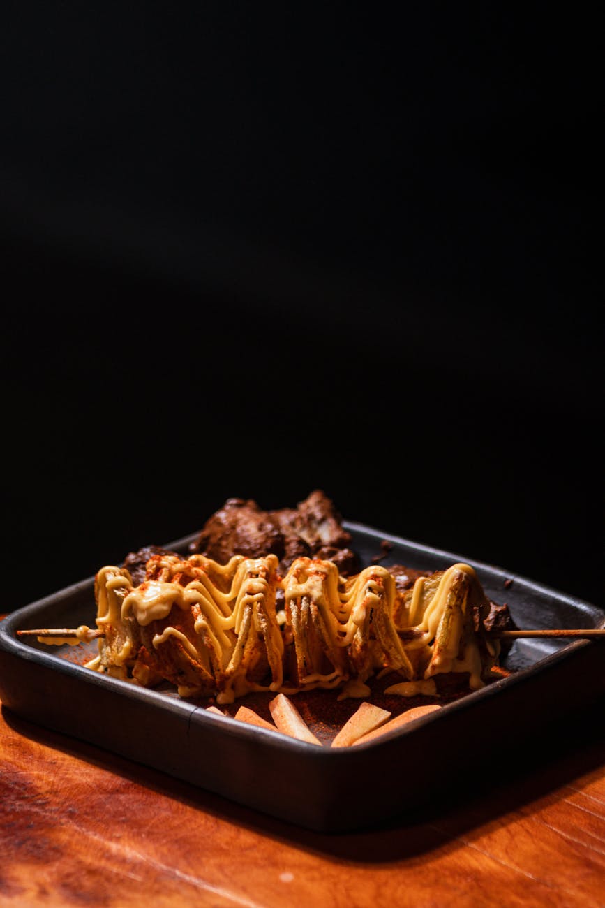 Tasty meat skewers topped with sauce, served with crispy fries in a dark setting.