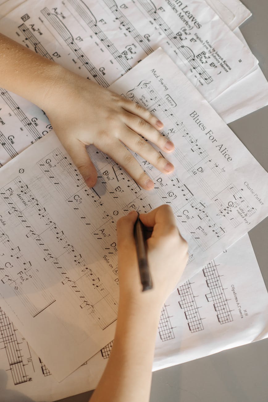 Hands writing chords on sheet music, top view of musical notes being edited.