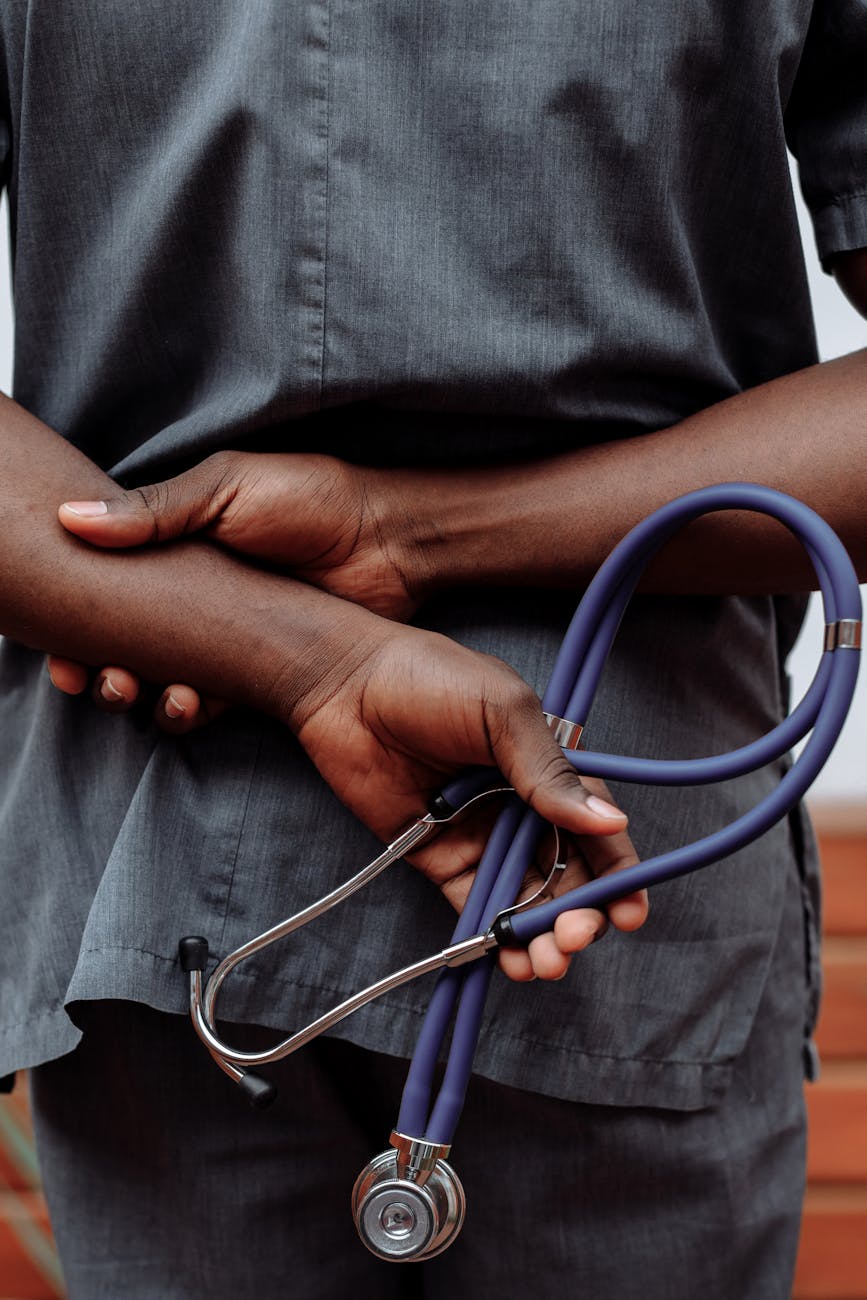 Medical professional in gray scrubs holding stethoscope behind back.