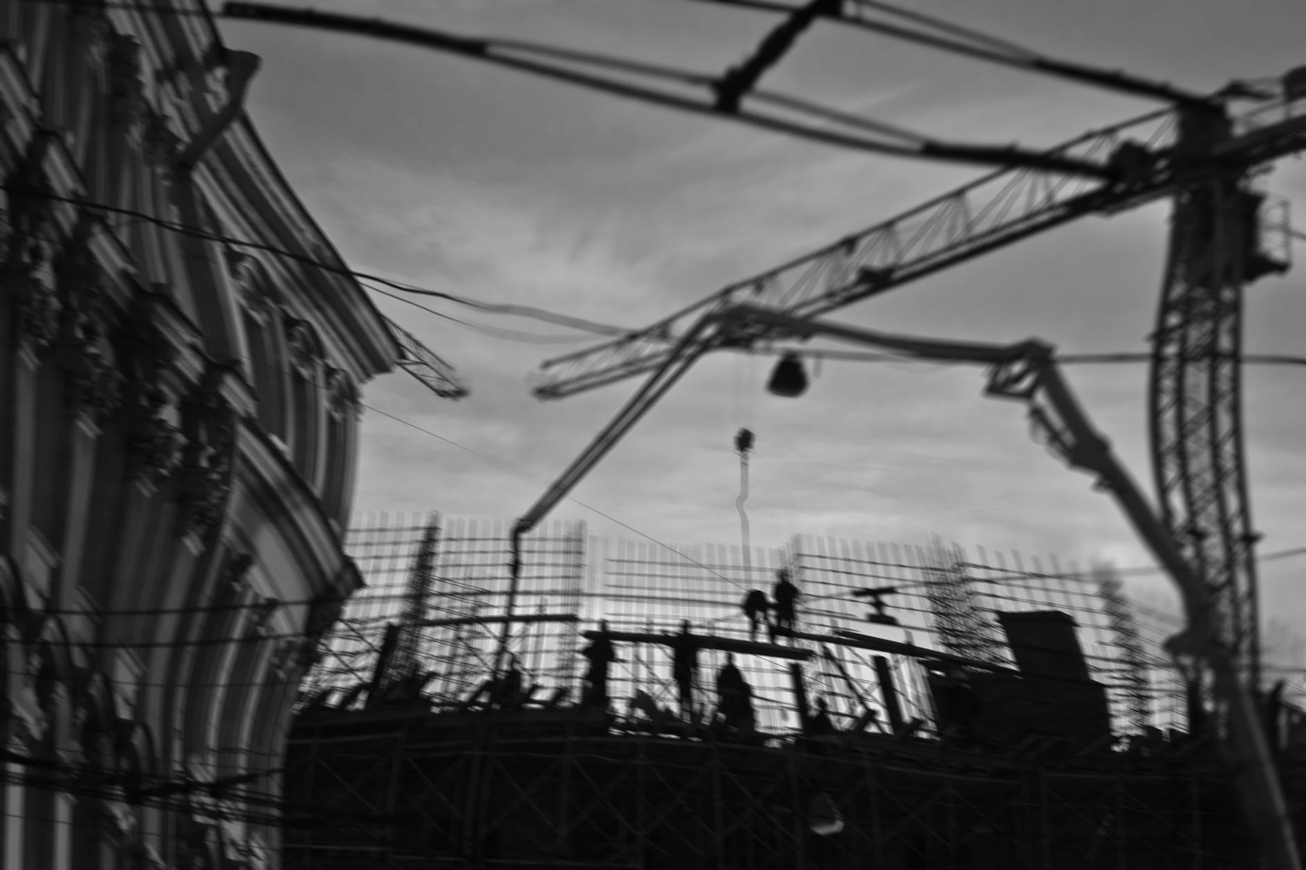 Silhouetted construction workers on site with cranes and scaffolding in a city setting.