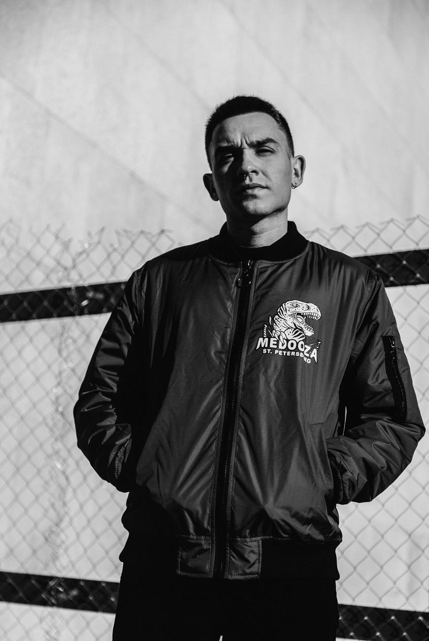 Monochrome image of a man in a jacket standing with a serious expression.