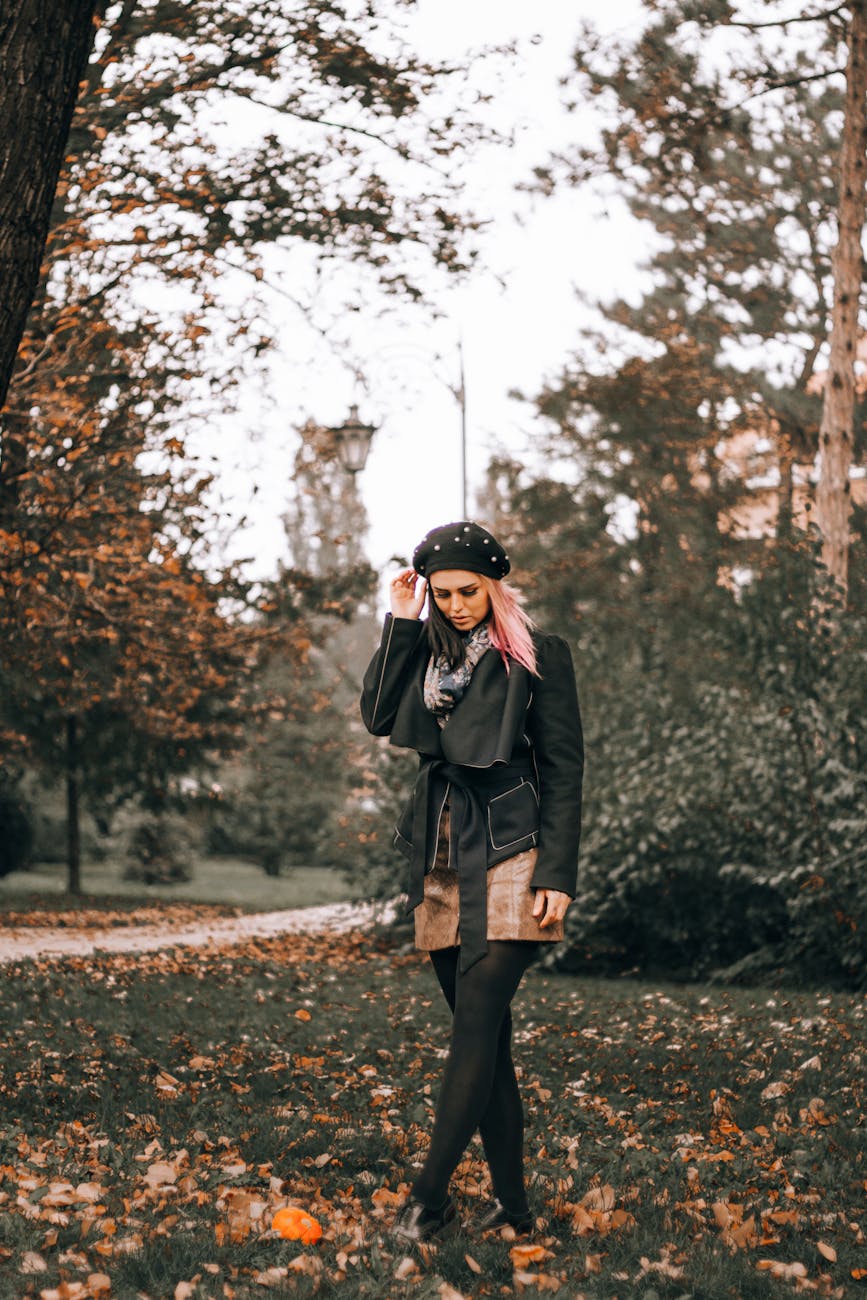 Woman in stylish autumn attire walking in a leafy park.