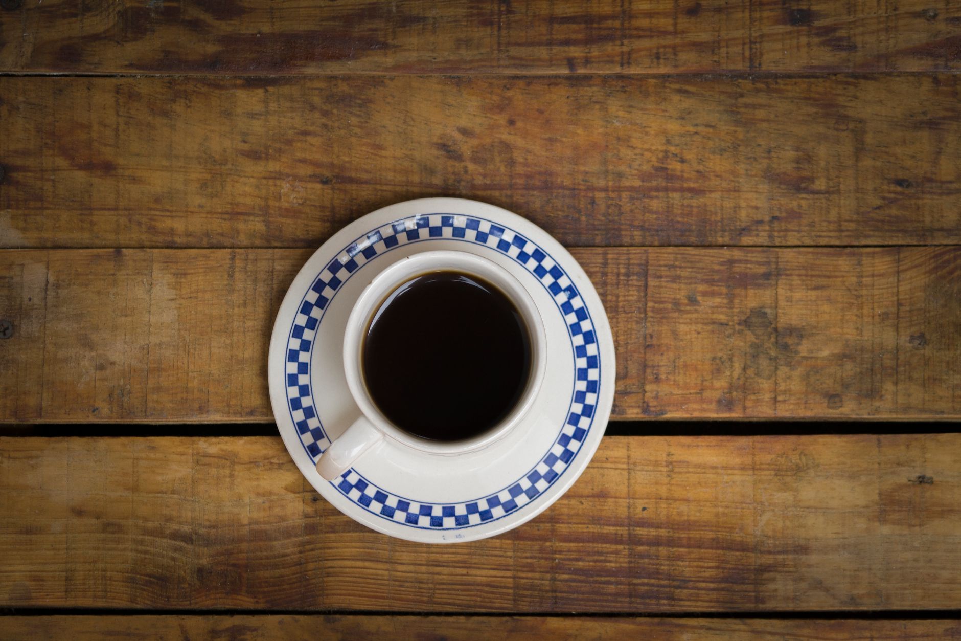 Aerial view of a coffee cup with a checkered saucer on a rustic wooden table.