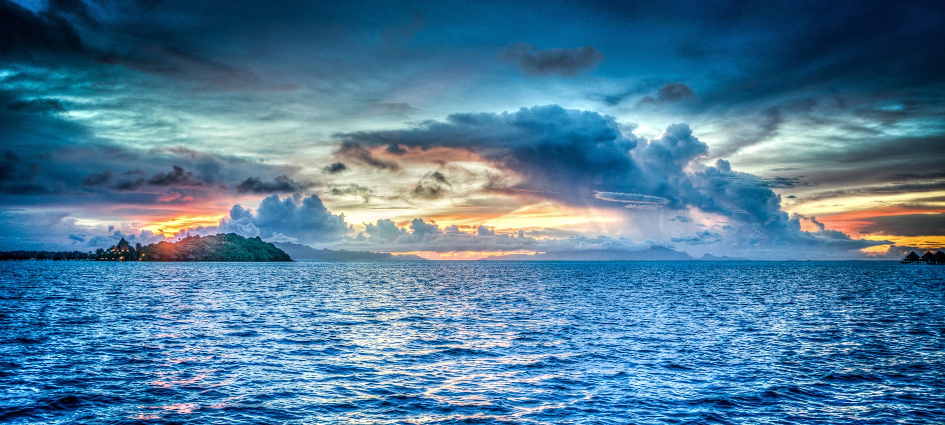 Vibrant sunset over tropical ocean with dramatic clouds and distant island.