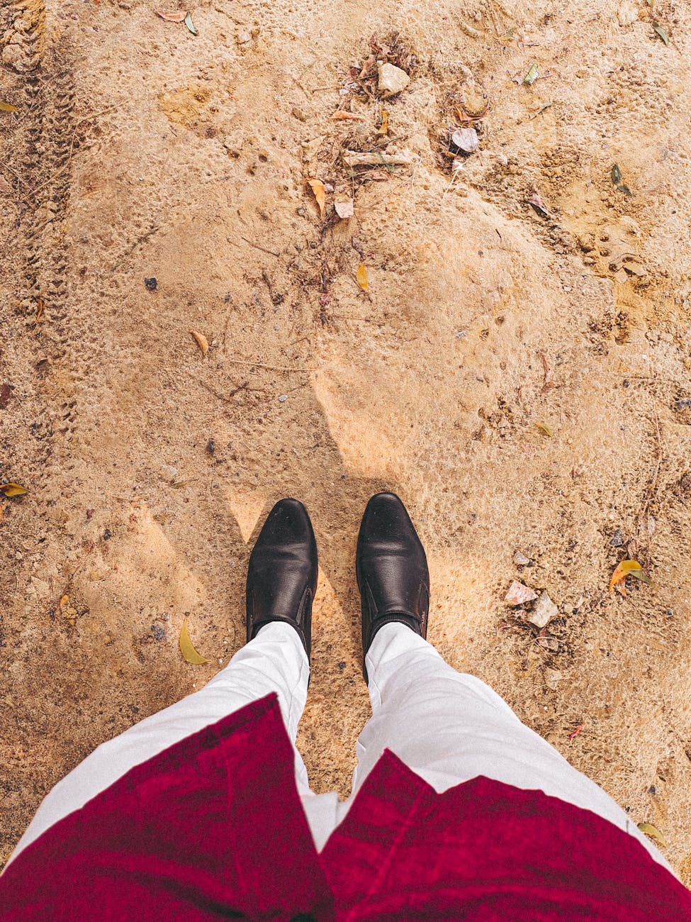 Elegant black shoes and white pants create a minimalist style against a sandy background.