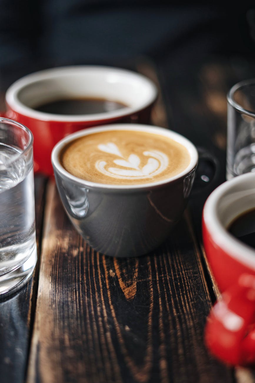 Close-up of latte art with cups of coffee and water on a rustic wooden table.