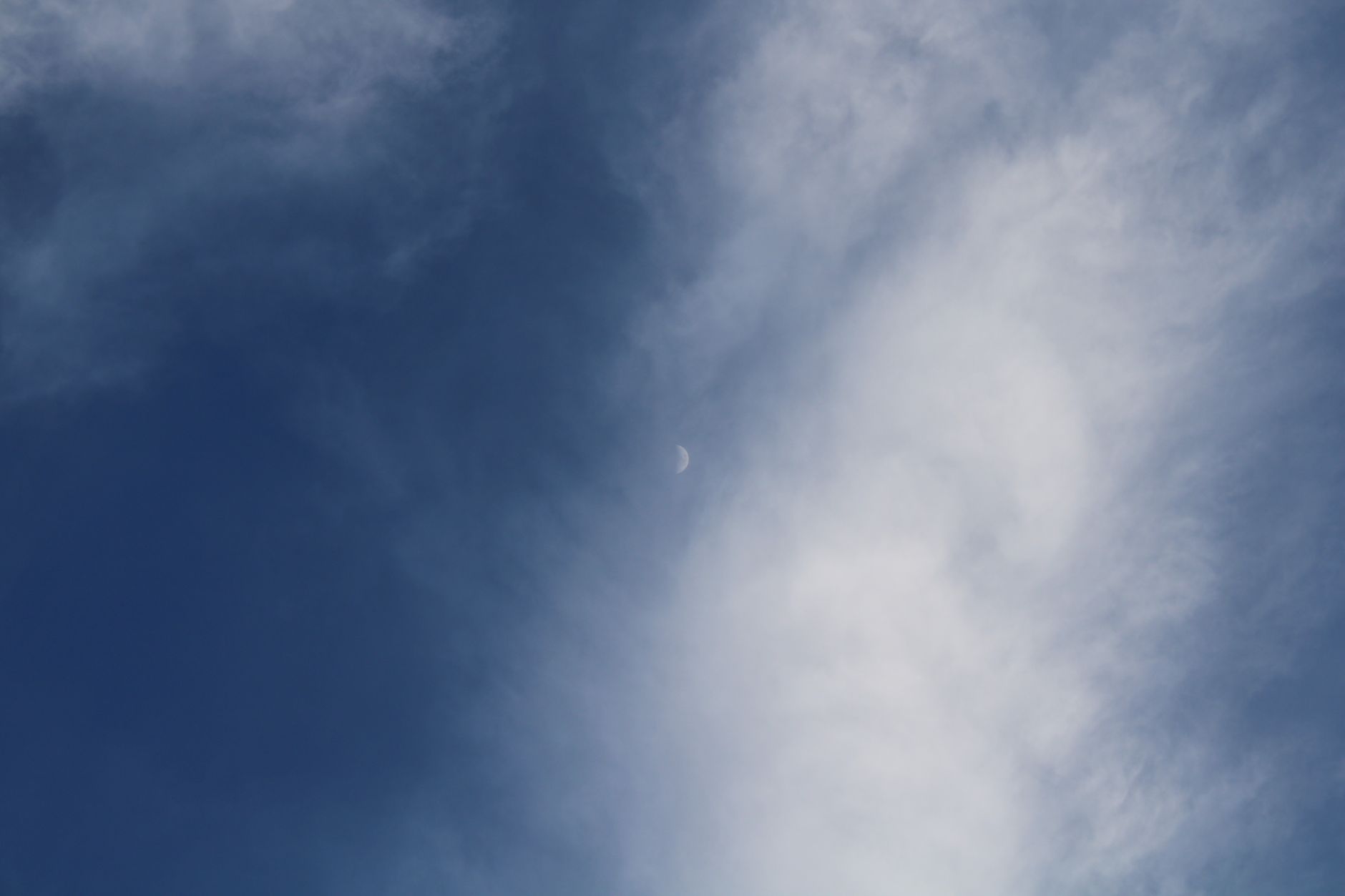 A serene daytime sky with white clouds framing a crescent moon.