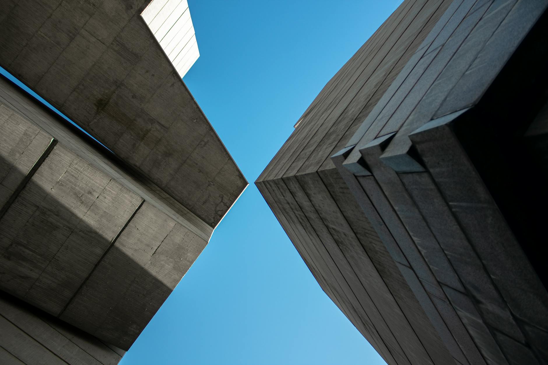 Low-angle view of modern concrete buildings against blue sky, showcasing abstract architectural design.