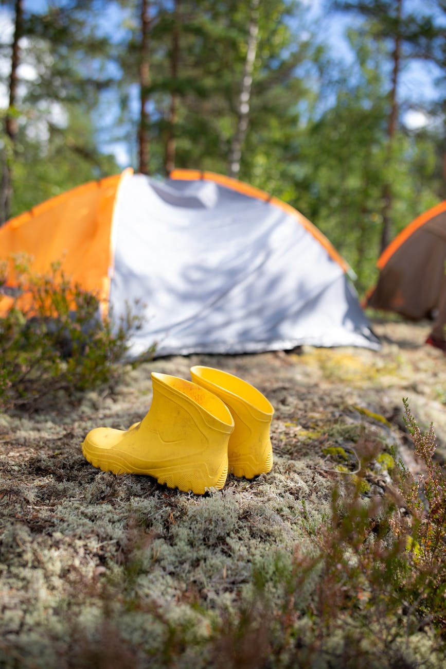 Bright yellow boots outside an orange tent in a lush wooded campsite, perfect for summer adventures.