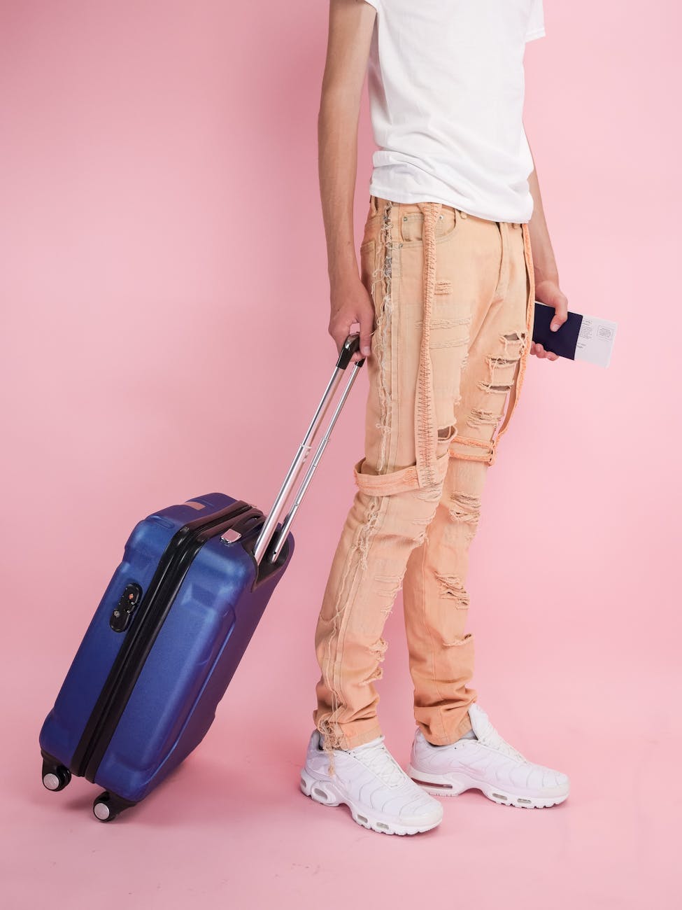 Stylish traveler with a blue suitcase and passport on a pink background.