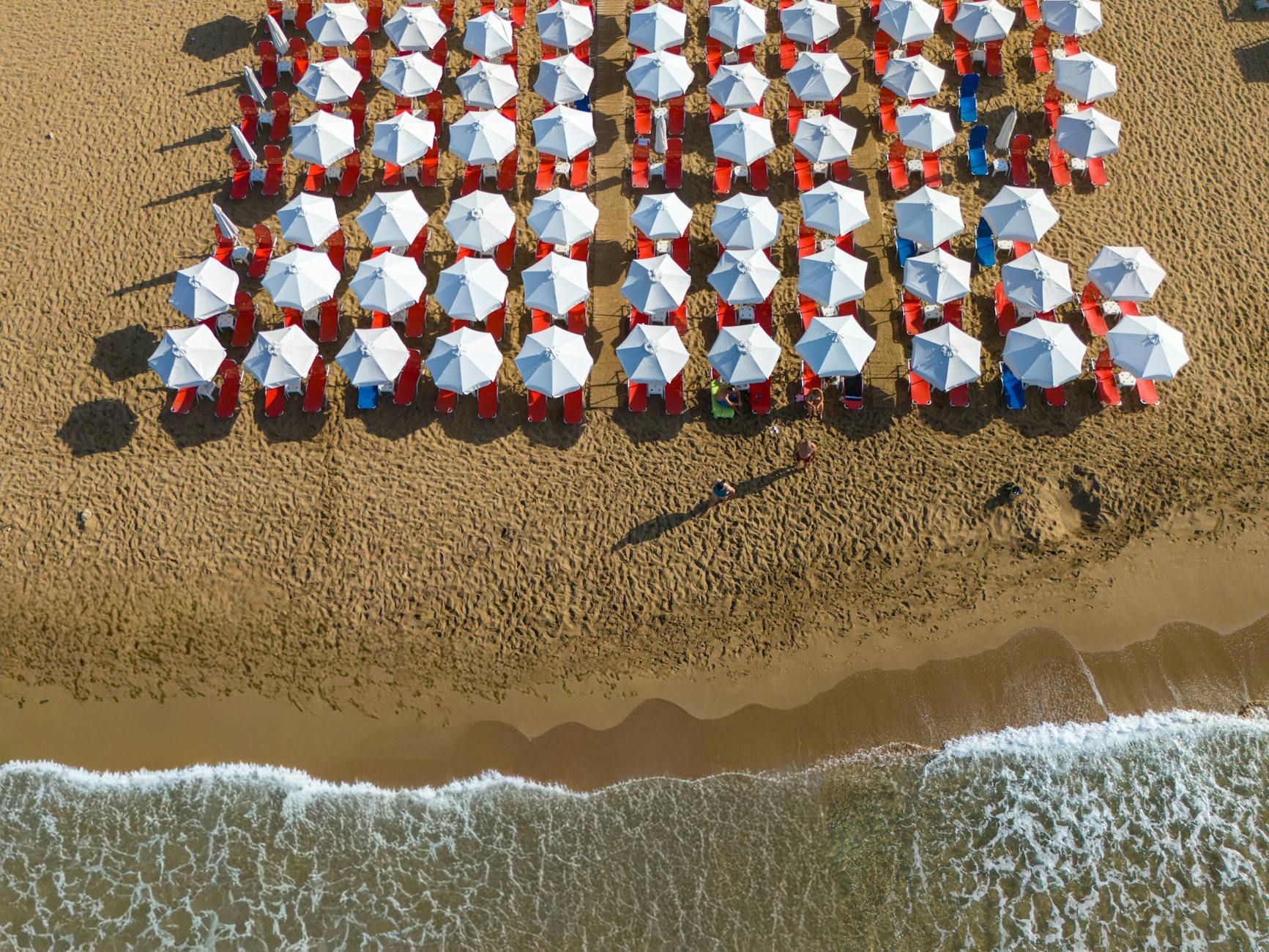 High-angle shot of aligned beach umbrellas on a sandy Greek beach by the Ionian Sea.
