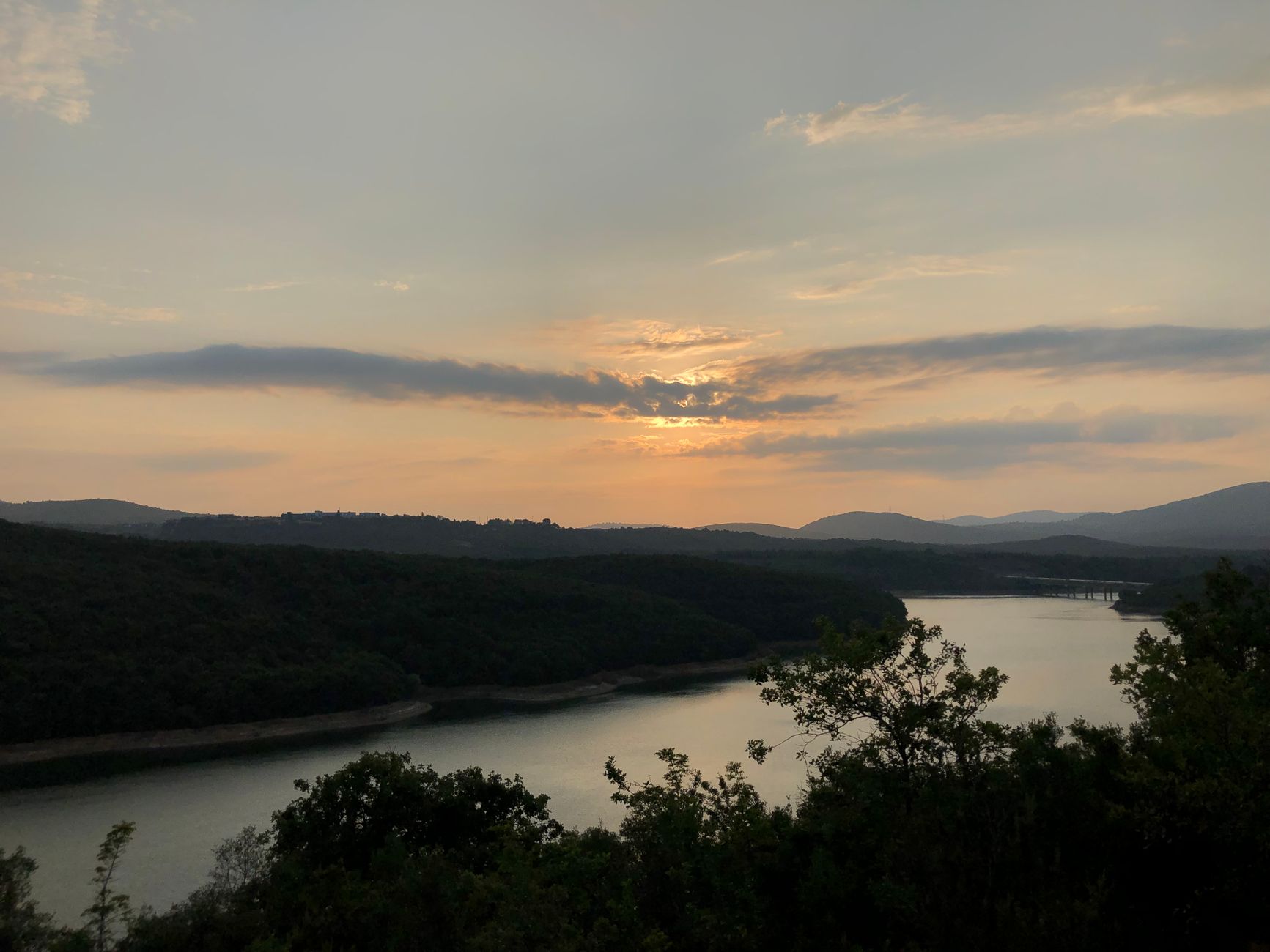 Beautiful sunset over a tranquil river surrounded by lush forests and hills.