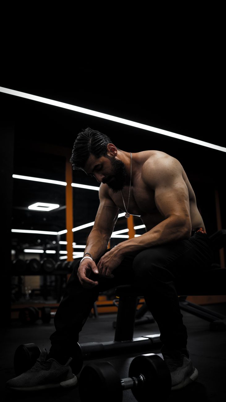 A muscular man sitting in a gym, exuding strength and contemplation.