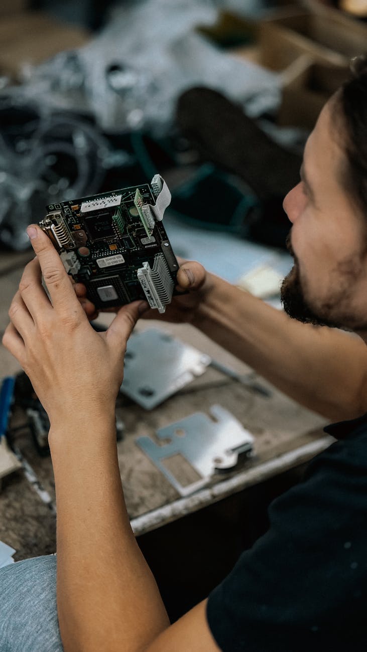 Focused technician examining a circuit board with precision in a cluttered workshop environment.