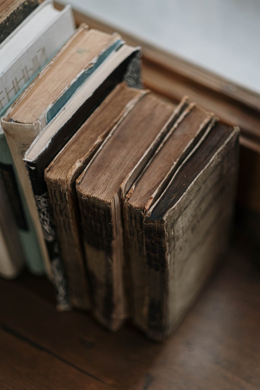 A vertical close-up capturing a collection of old, worn books on a wooden surface.