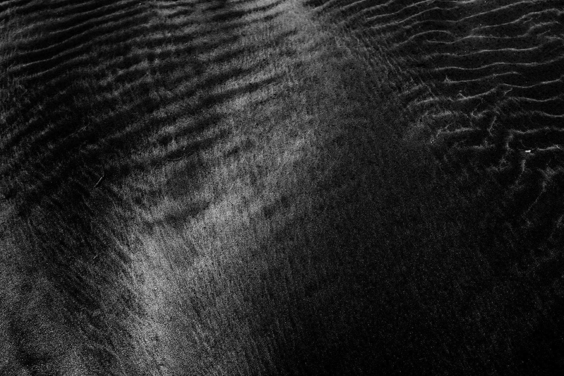 Detailed close-up of a black sand texture with smooth and patterned ripples.