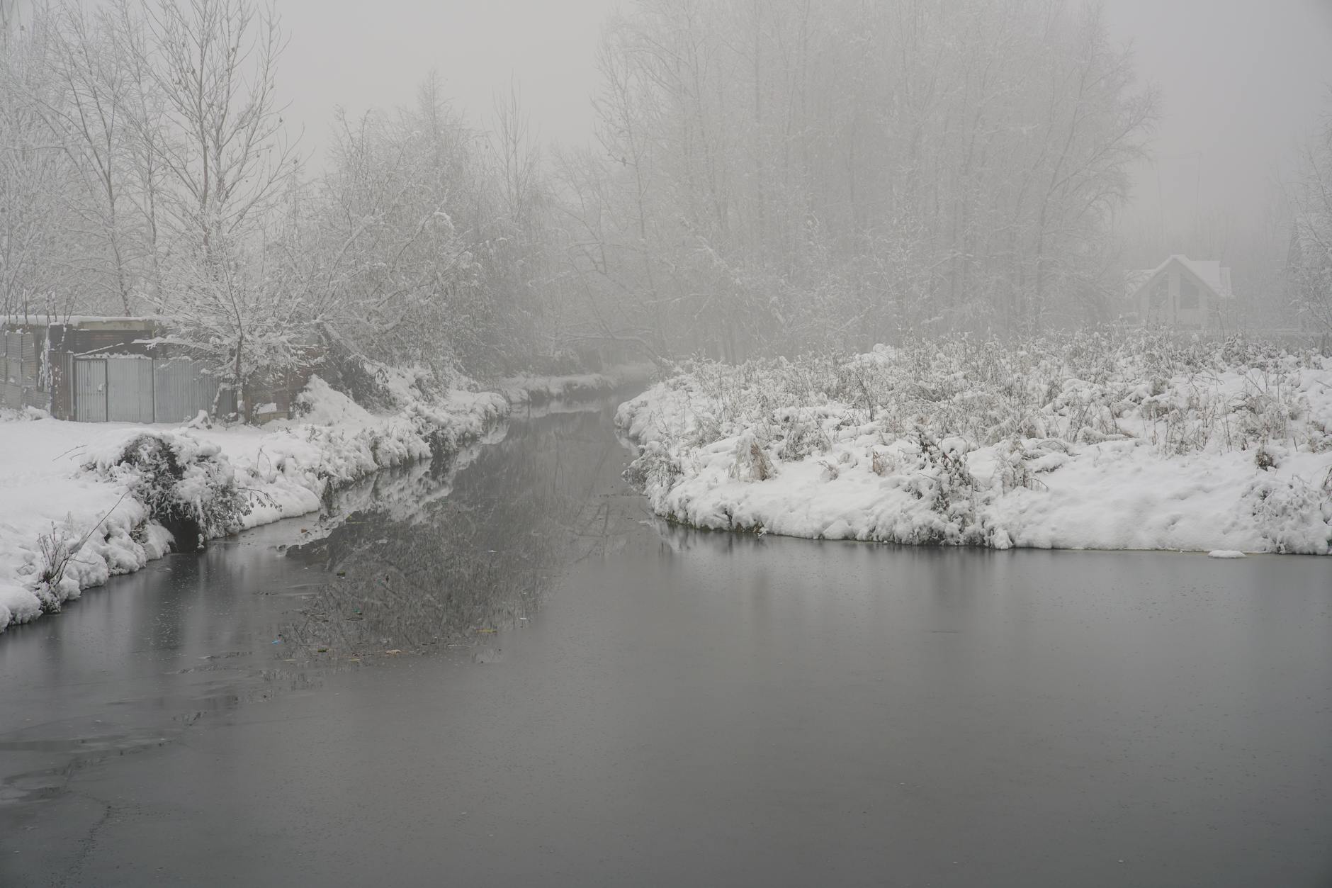 A tranquil snow-covered riverbank in Jammu and Kashmir, showcasing winter serenity.