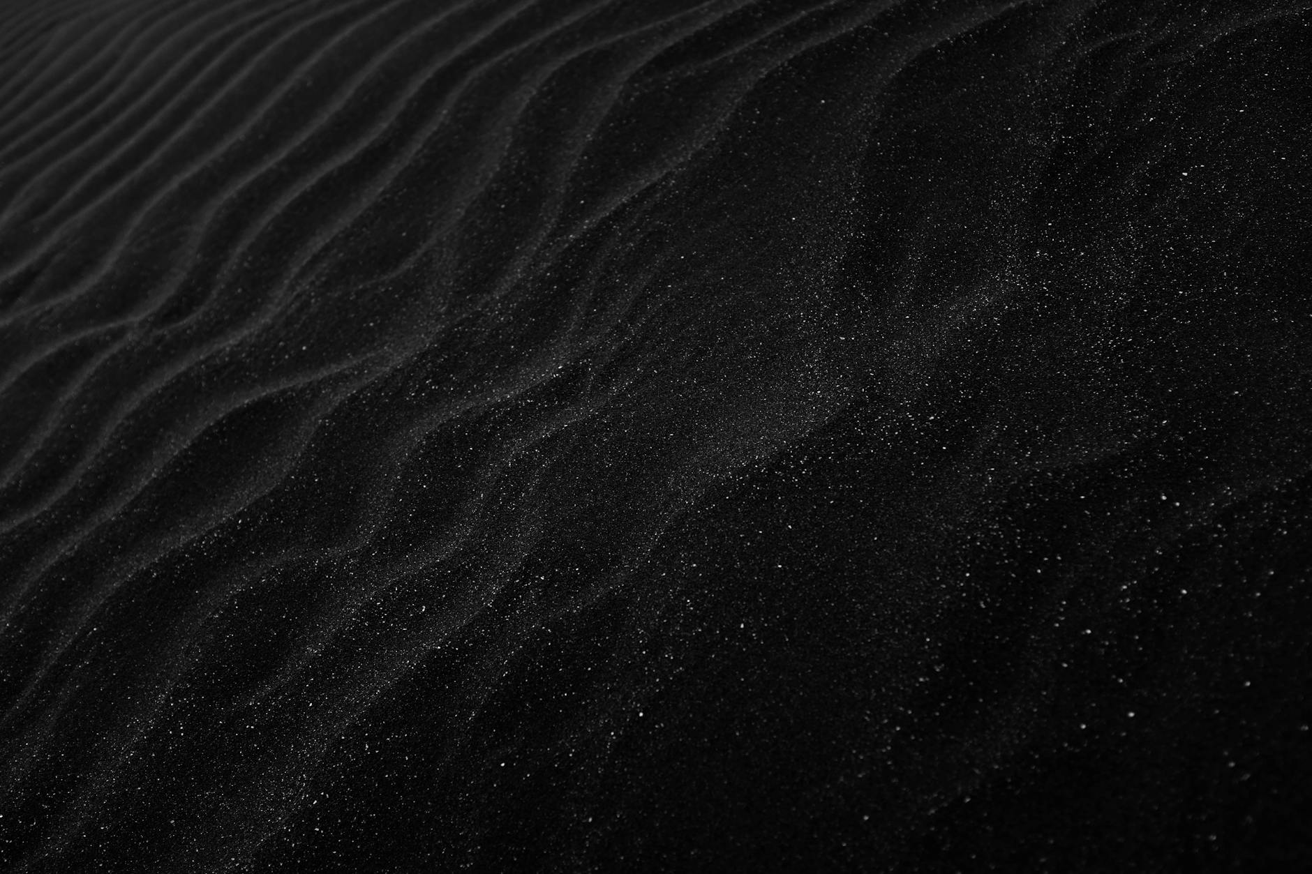 Textured black sand with ripples resembling dunes, creating a dark, abstract aesthetic.