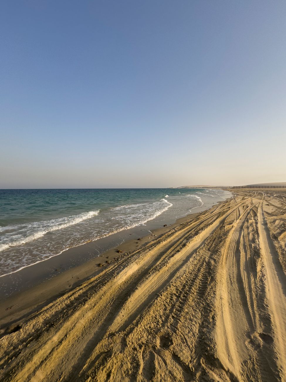 Tranquil beachscape with tire tracks along the shore at sunset, evoking a sense of adventure and solitude.