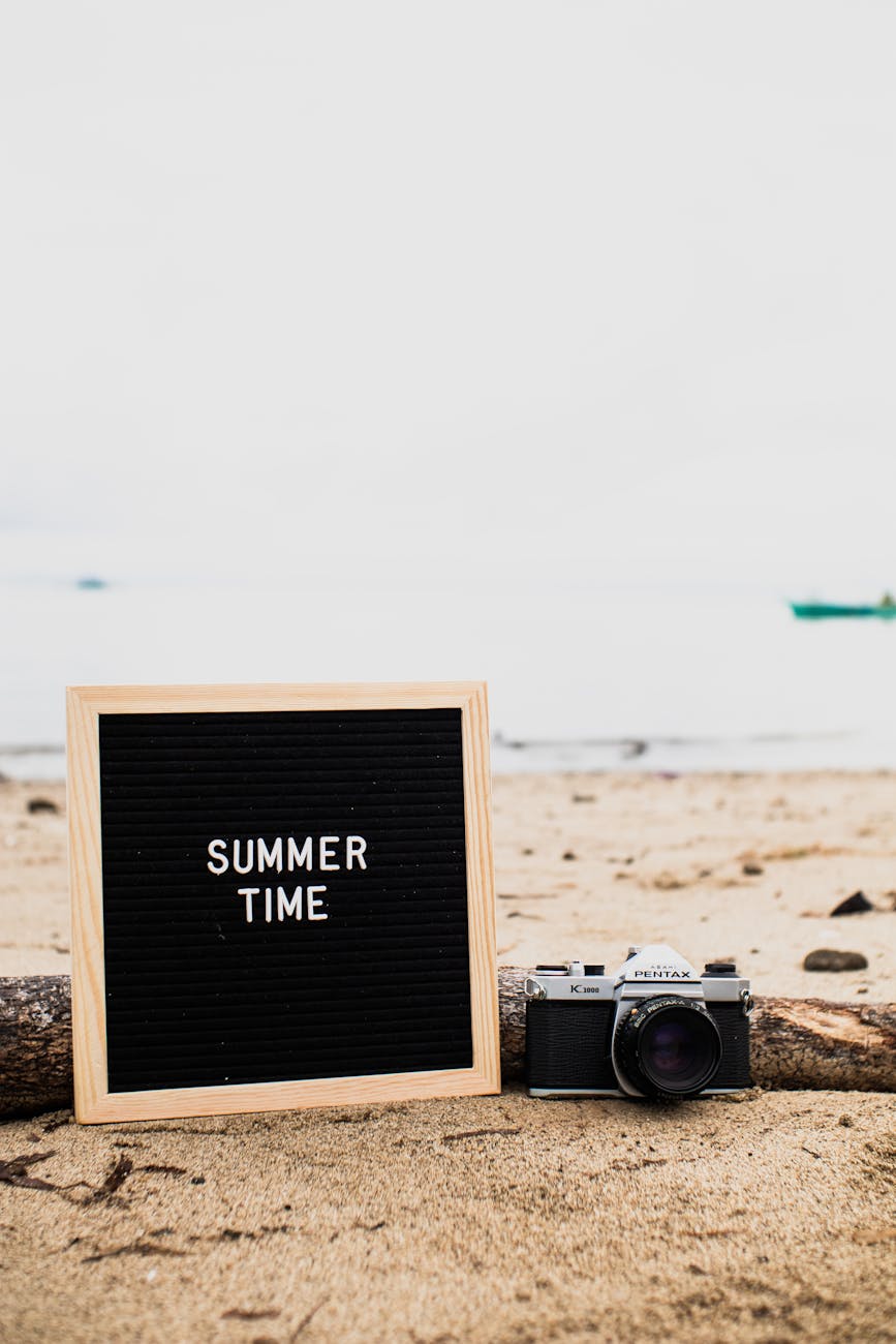 A vintage camera and summer sign on a sandy beach, perfect for travel inspiration.