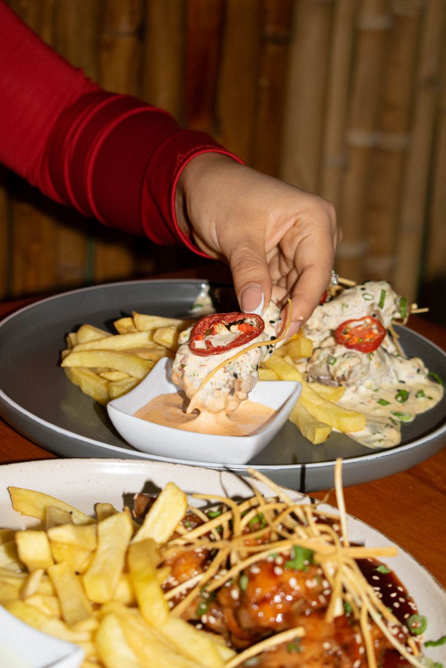 Hand picking a tasty chicken piece with fries and creamy dipping sauce in a cozy setting.