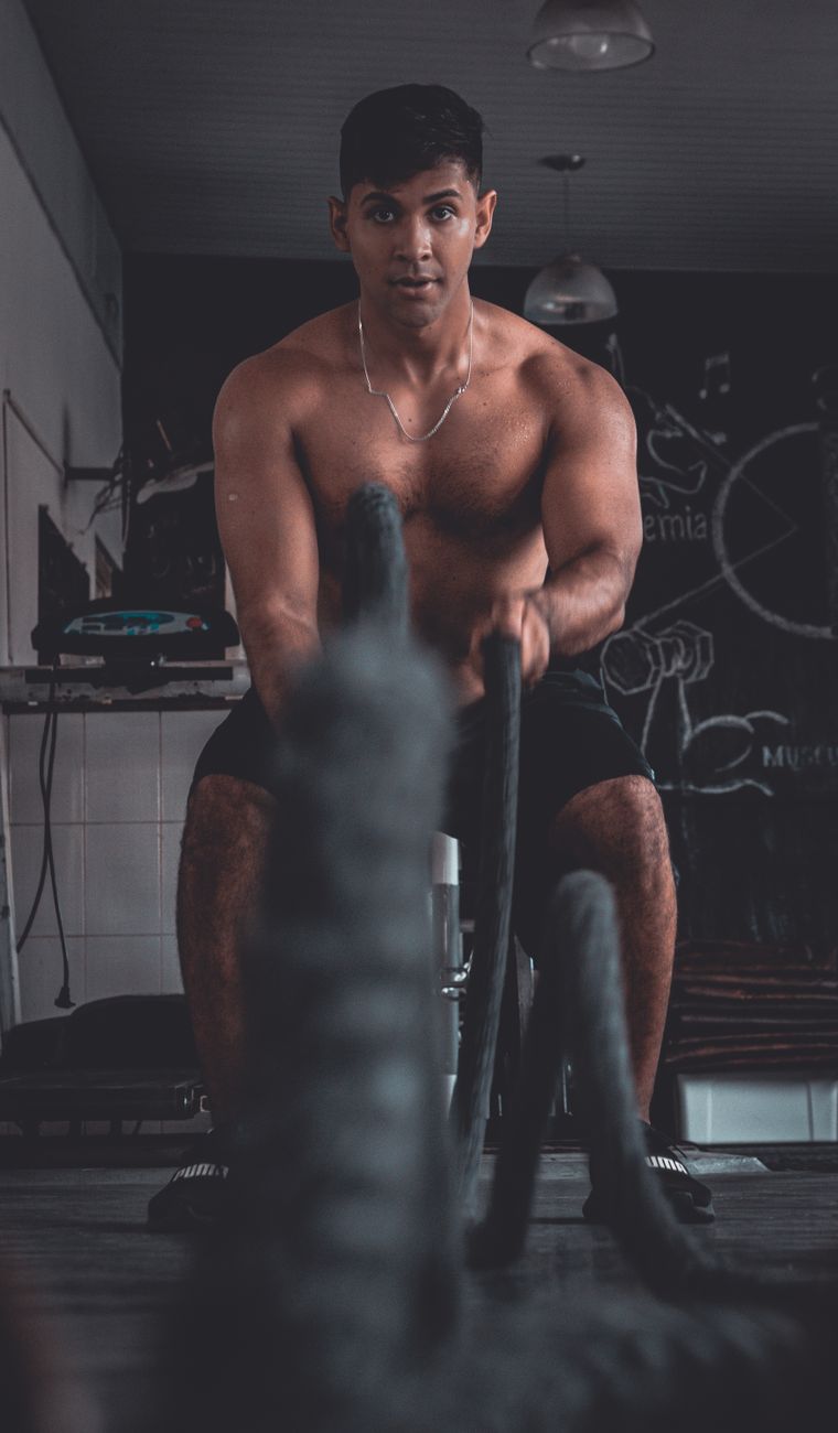 Fit young man working out with battle ropes in a gym setting.