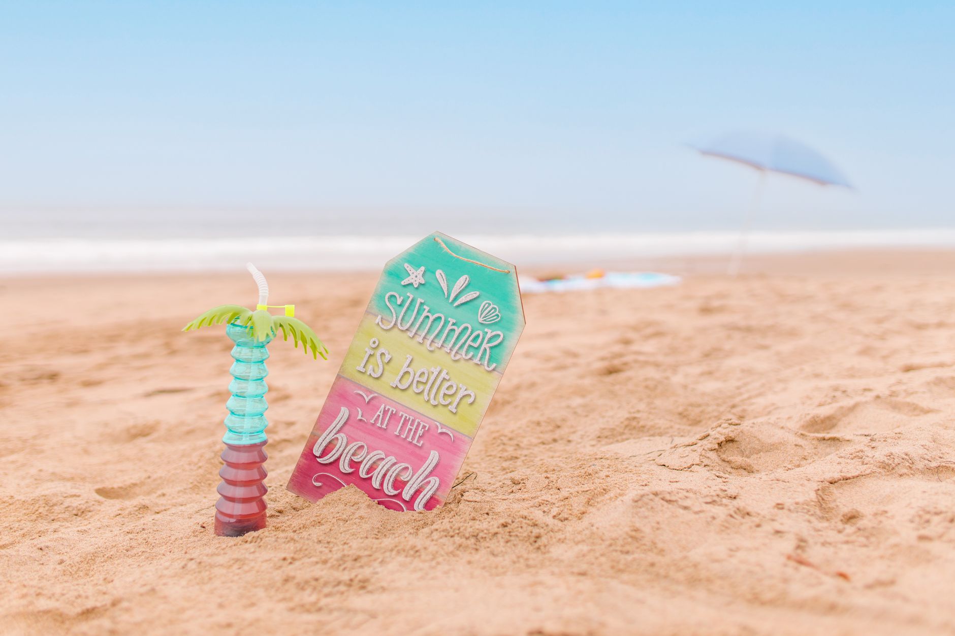 Vibrant beach scene with a tropical drink and 'Summer is better at the beach' sign.