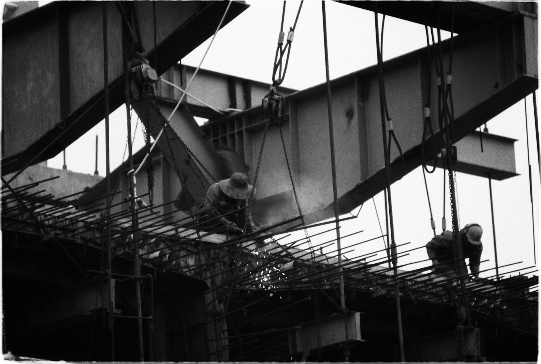 Black and white photo of construction workers welding on a steel structure at a high-rise building site.