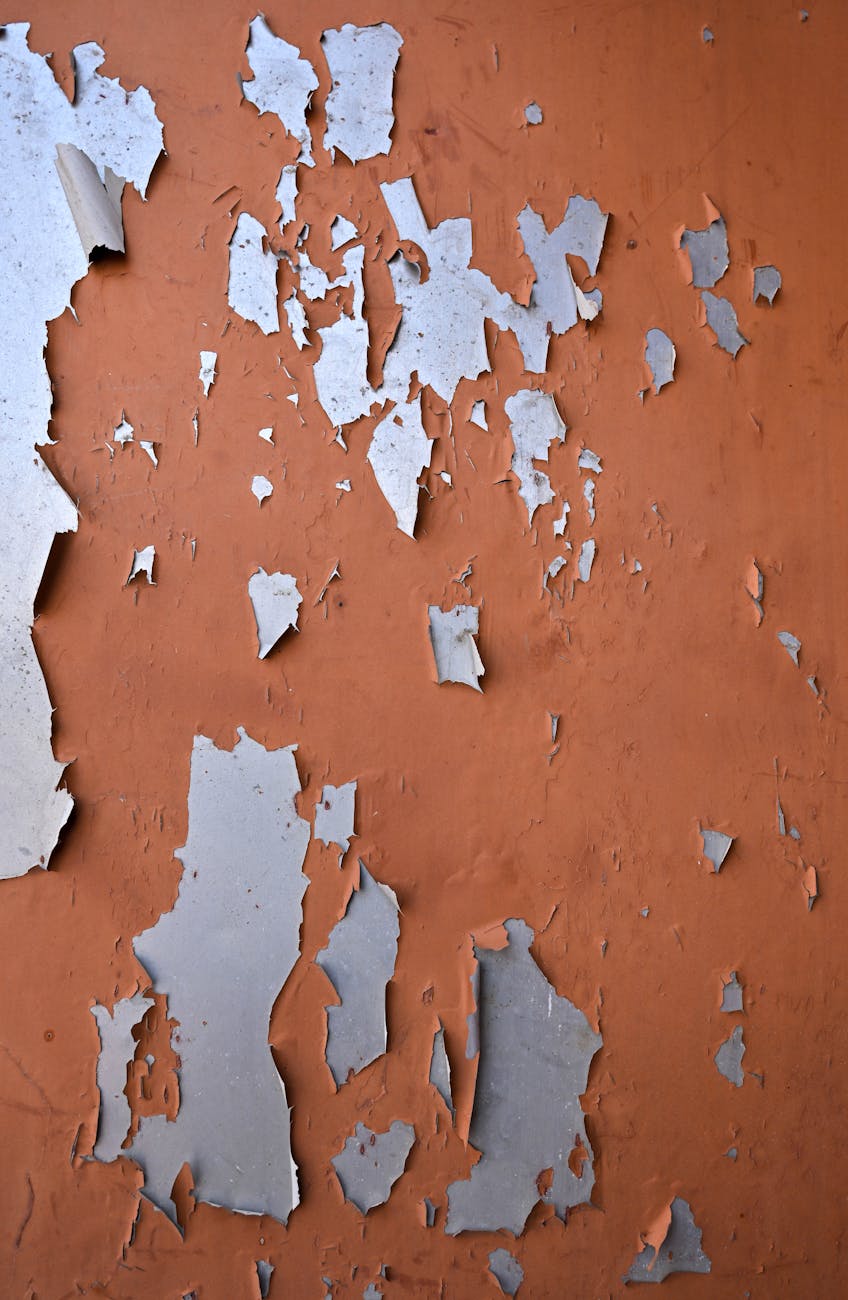 Close-up of weathered and peeling paint on an orange wall, showcasing urban decay and rustic textures.