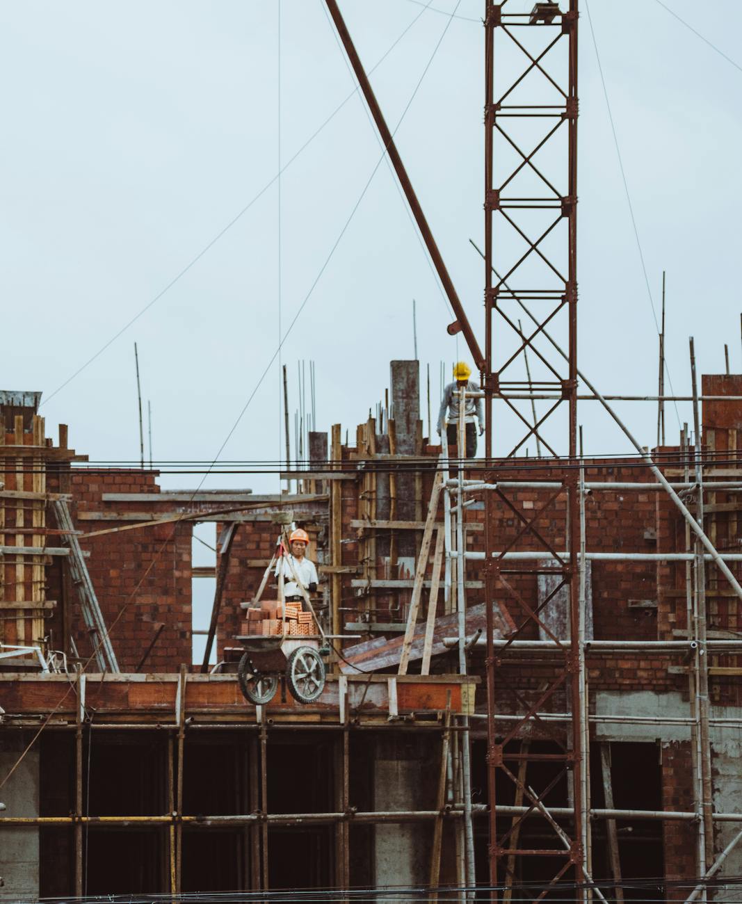 A construction worker on a scaffold at a building site with cranes and brickwork visible.