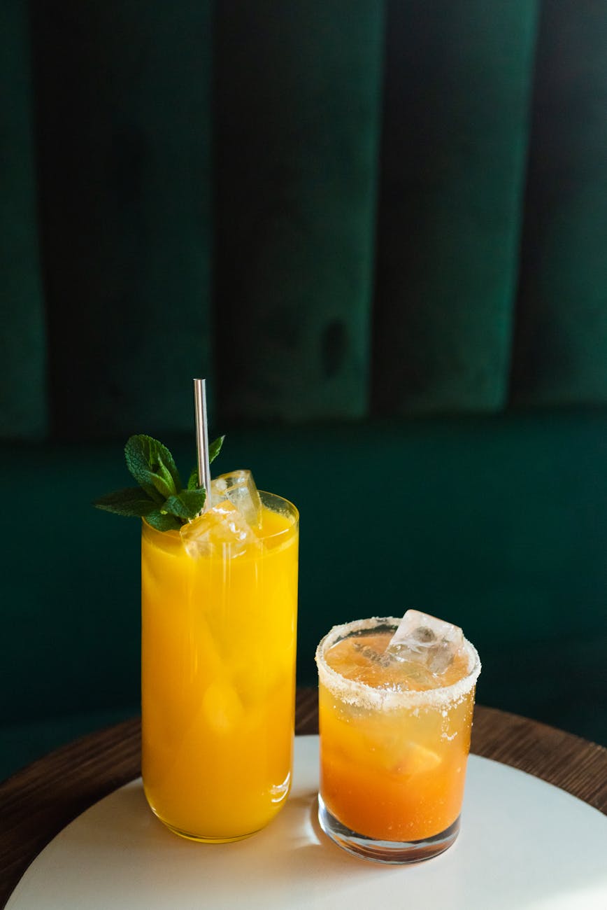 Bright citrus cocktails with ice, garnished with mint leaves, on a stylish indoor setting.