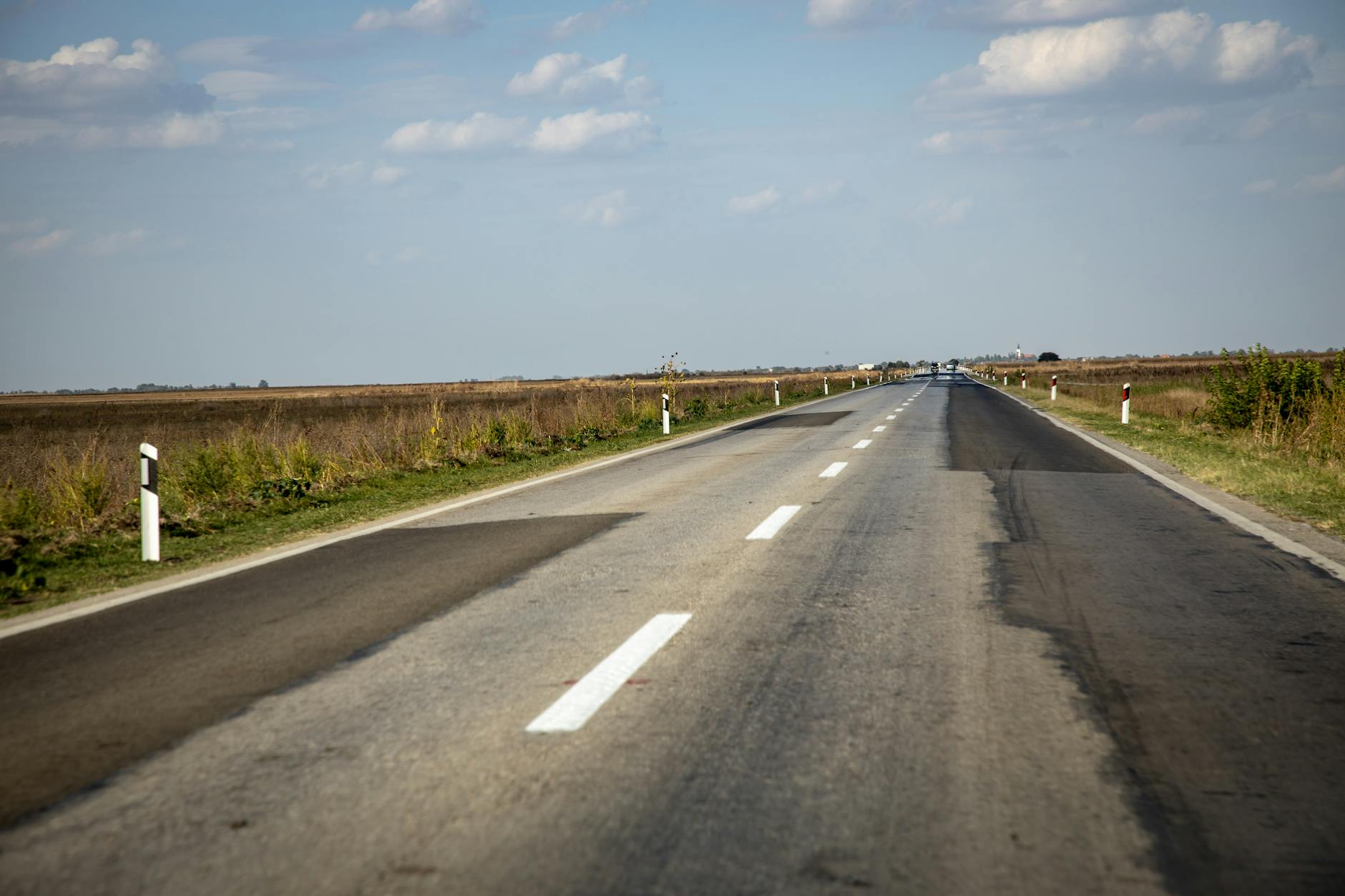 A long, straight rural road vanishing into the horizon under a blue sky.