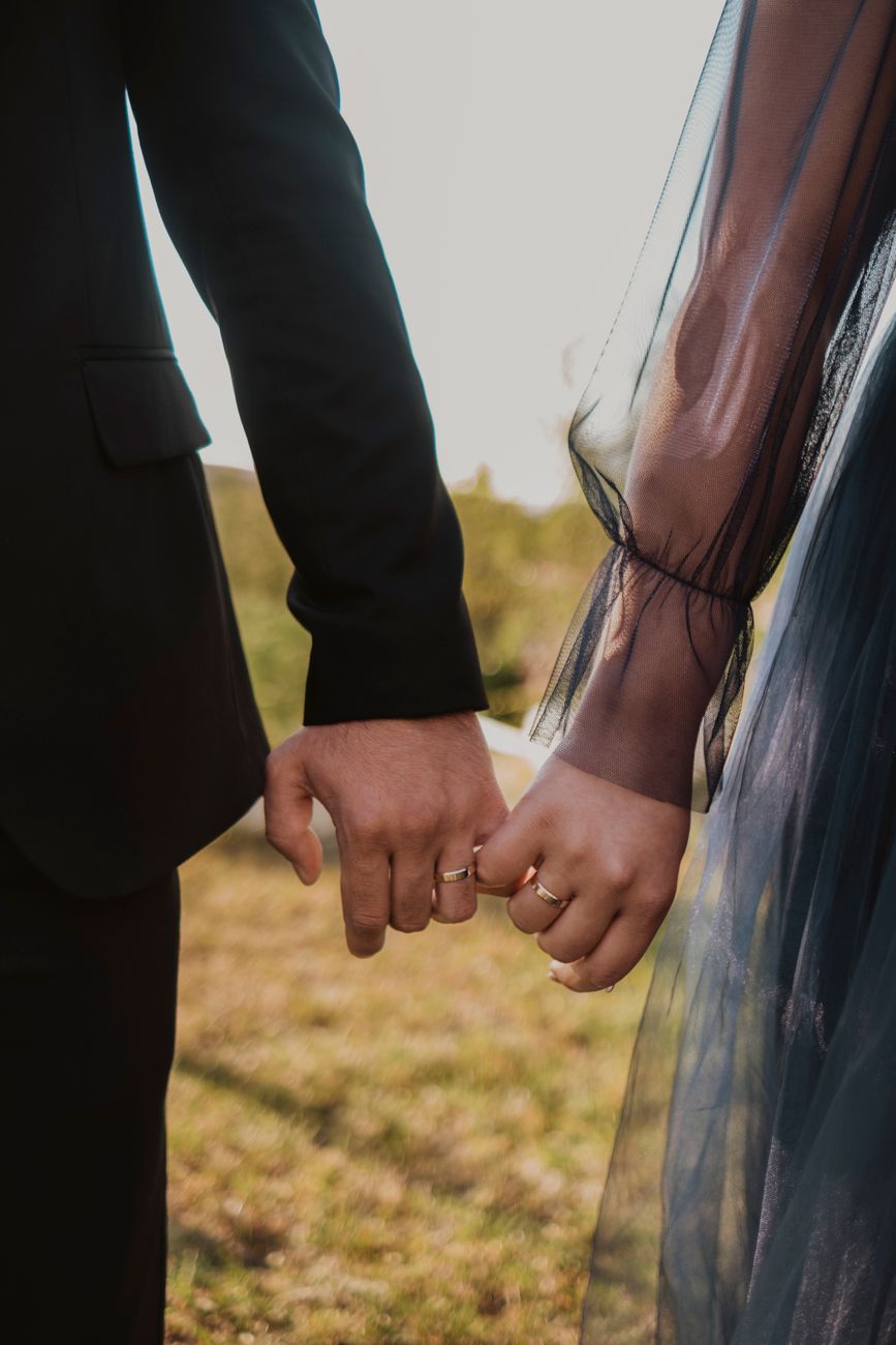 A newlywed couple holds hands displaying their wedding rings in a romantic outdoor setting.