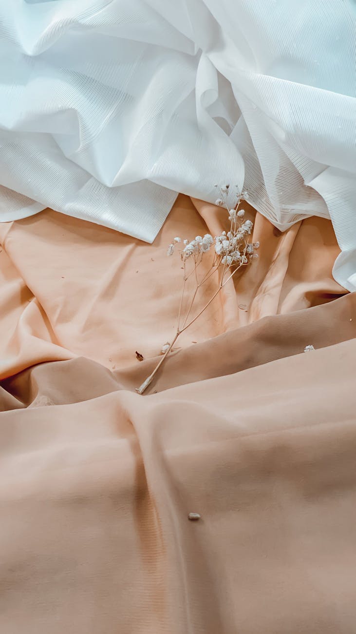 A still life of delicate white flowers resting on soft pink and white fabric.
