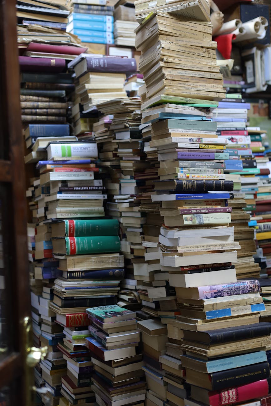 A cluttered bookstore filled with towering stacks of books in varied colors and sizes.