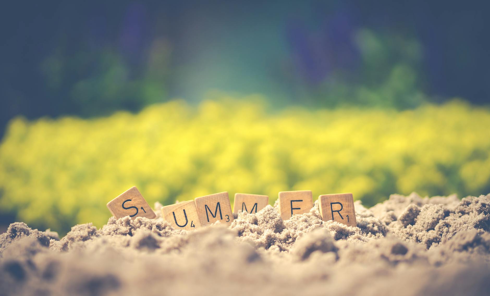 Scrabble tiles forming the word 'summer' in sand with a blurred background, evoking warm vibes.