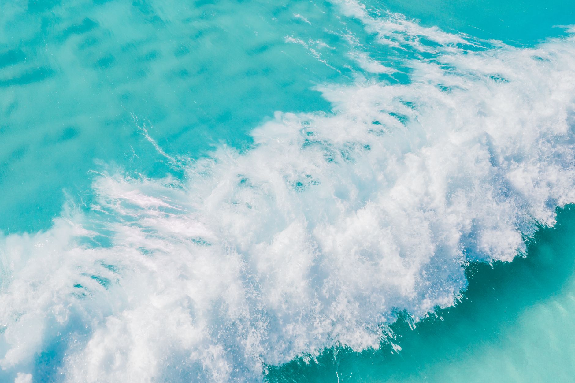 A stunning aerial shot of turquoise waves crashing in the vast ocean, creating a dynamic and vibrant natural scene.