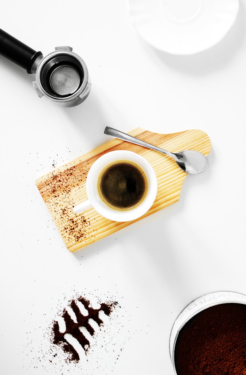 A fresh cup of black coffee on a wooden cutting board with coffee grounds and espresso tools.