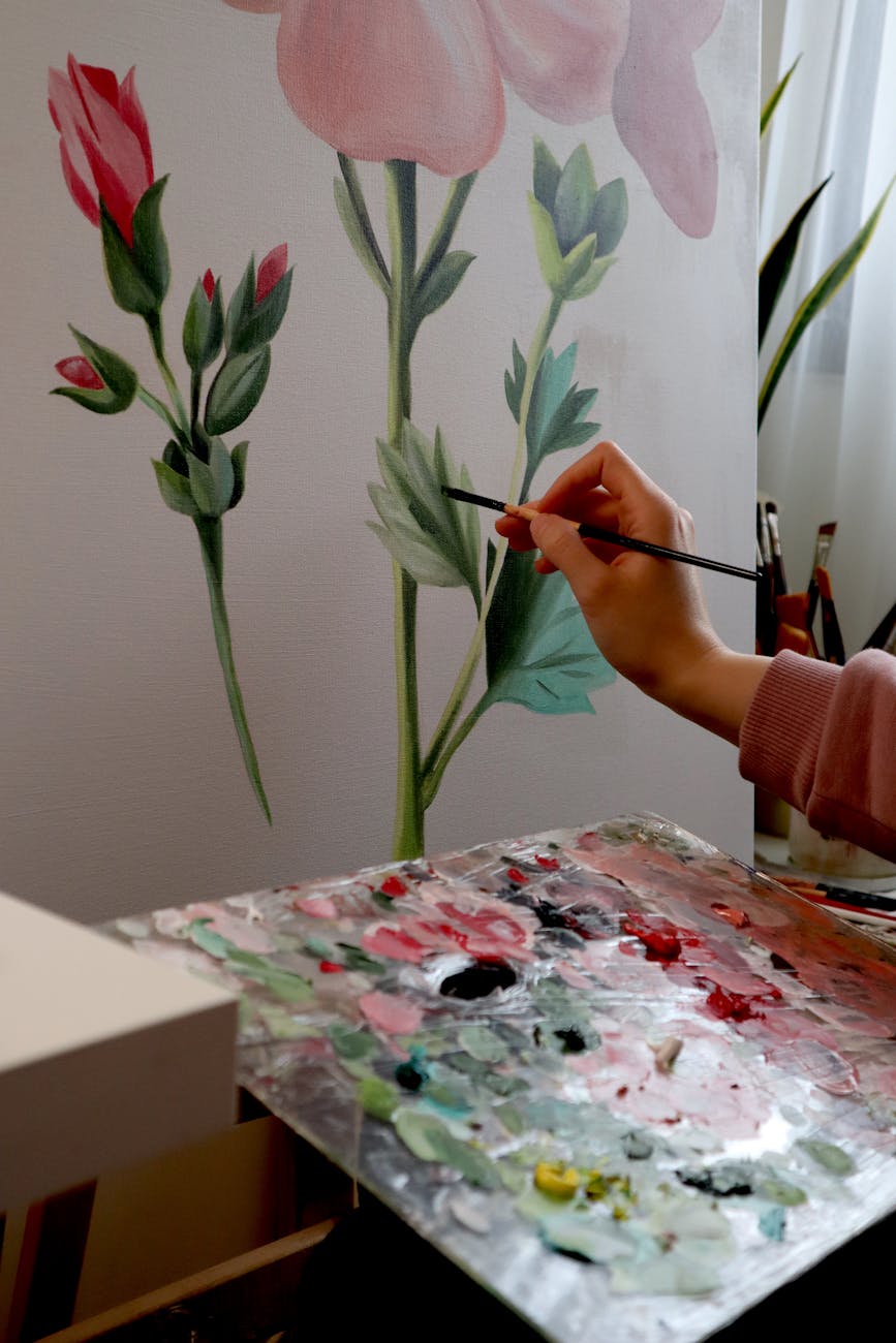 Artist painting flowers on canvas with palette, emphasizing creativity and artistry.